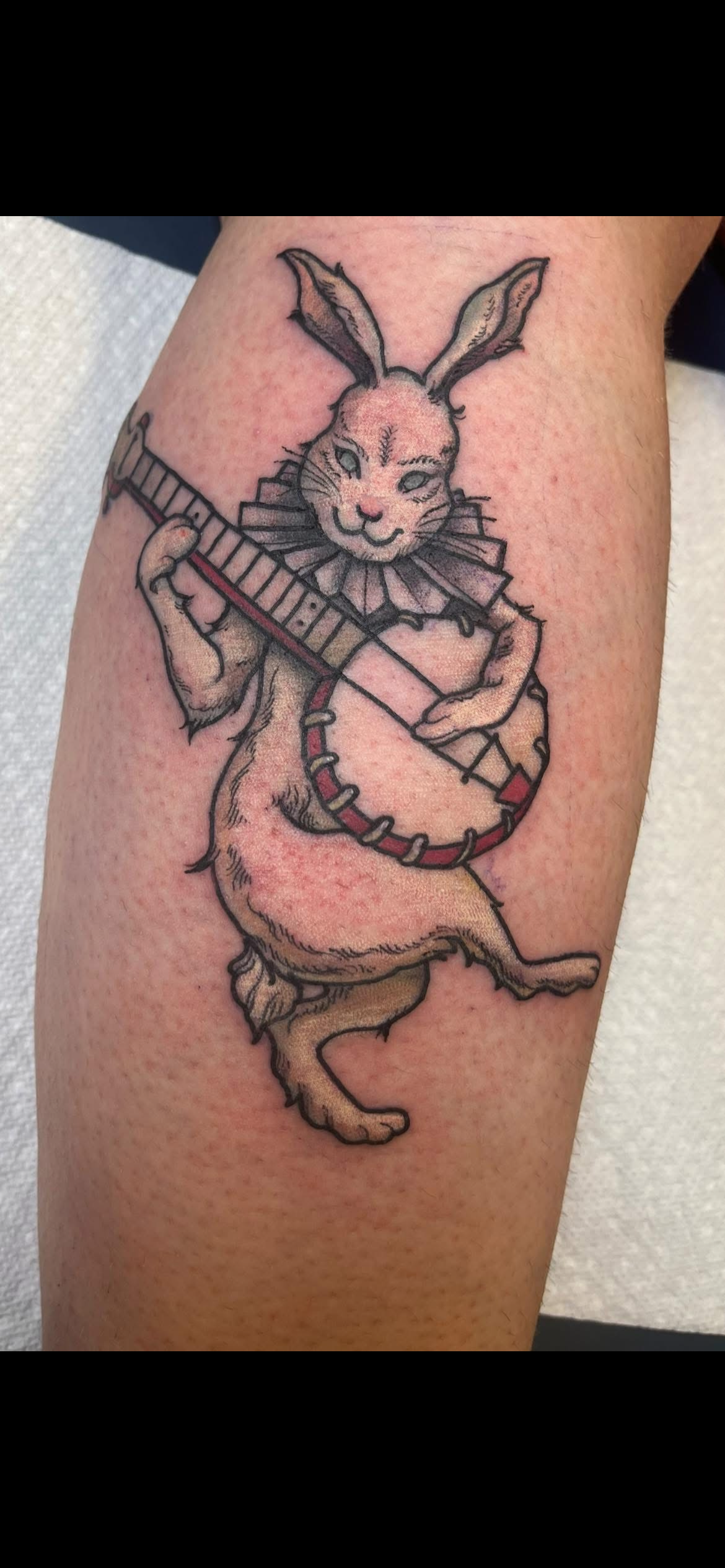 Tattoo of a rabbit with a ruffled collar playing a banjo.