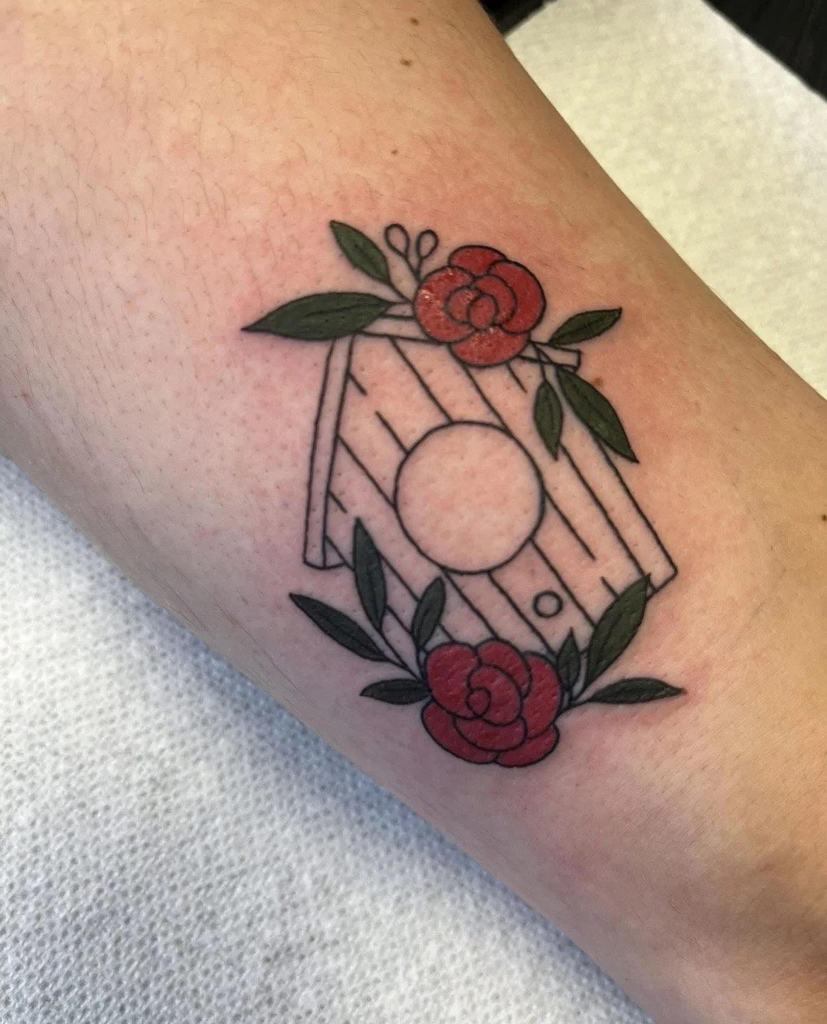 A tattoo of a Polaroid camera with floral decorations, featuring red roses and green leaves on the person's arm.