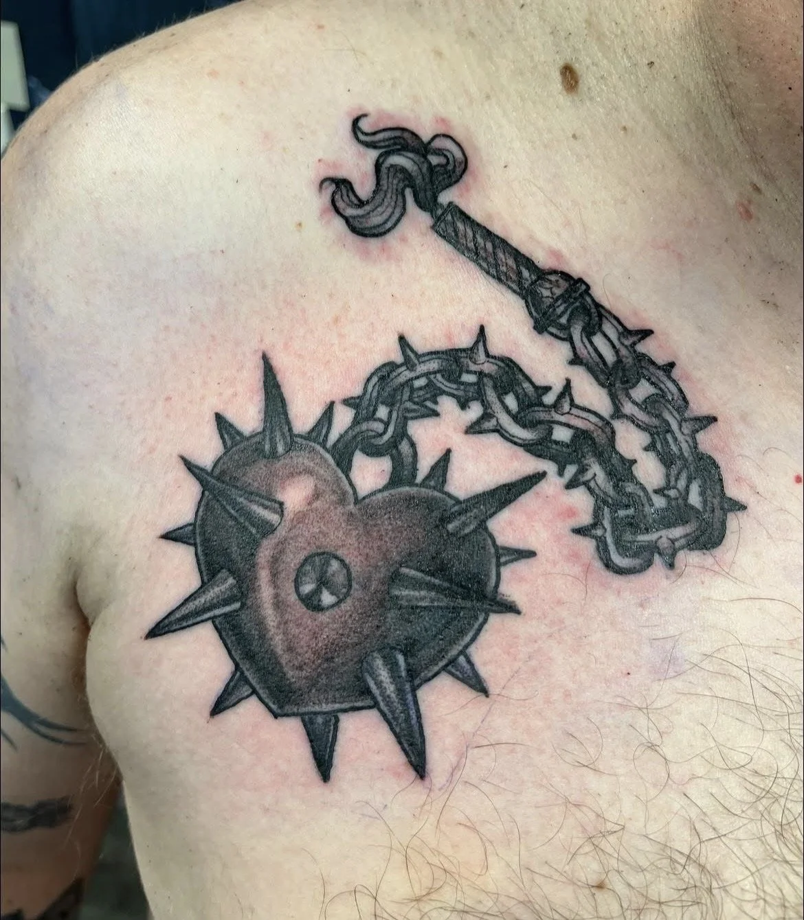 Tattoo of a medieval club and a spiked iron ball connected by a chain on a person's shoulder.
