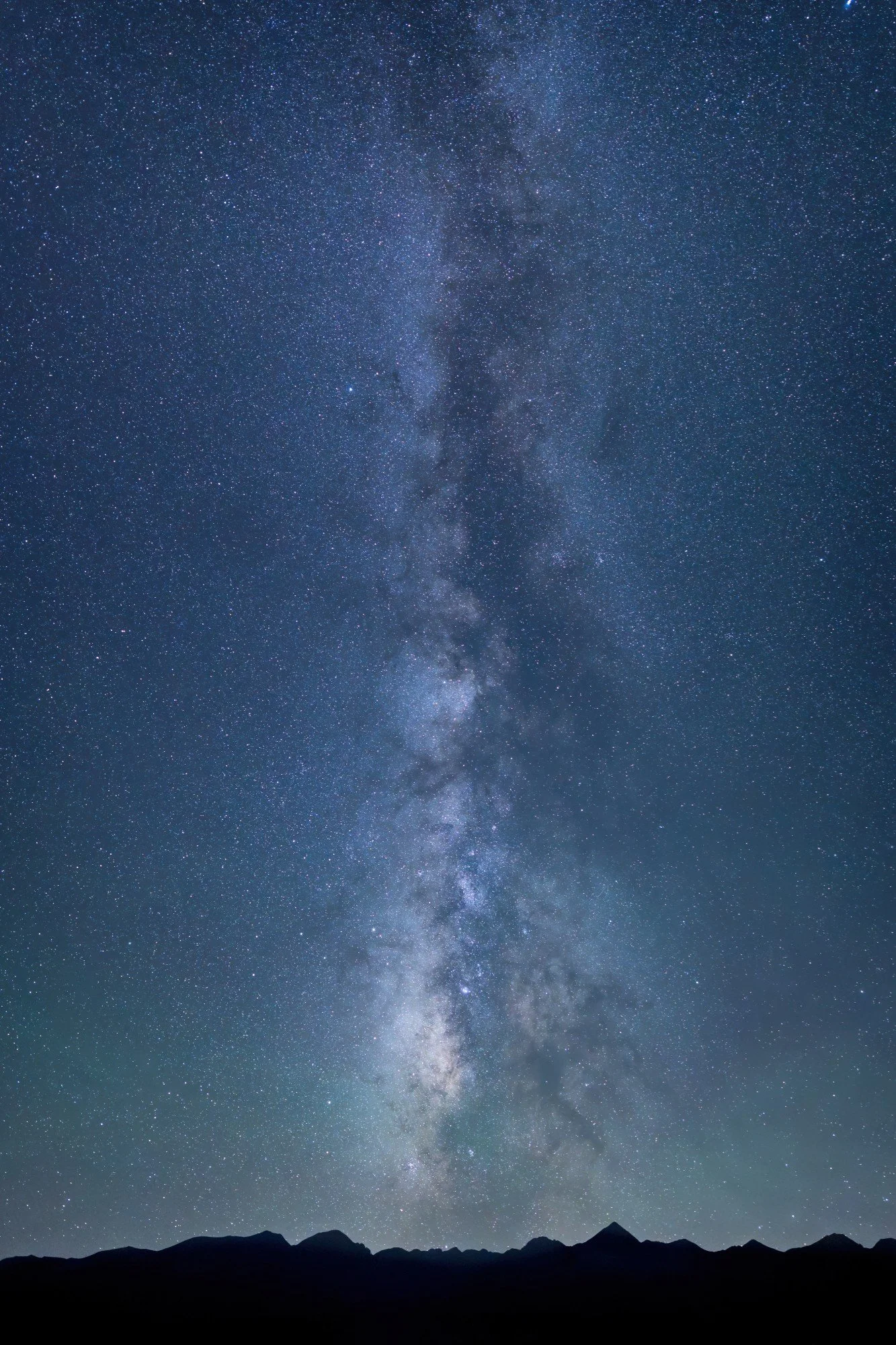 A clear night sky filled with stars and the Milky Way galaxy visible above a silhouette of mountain peaks.