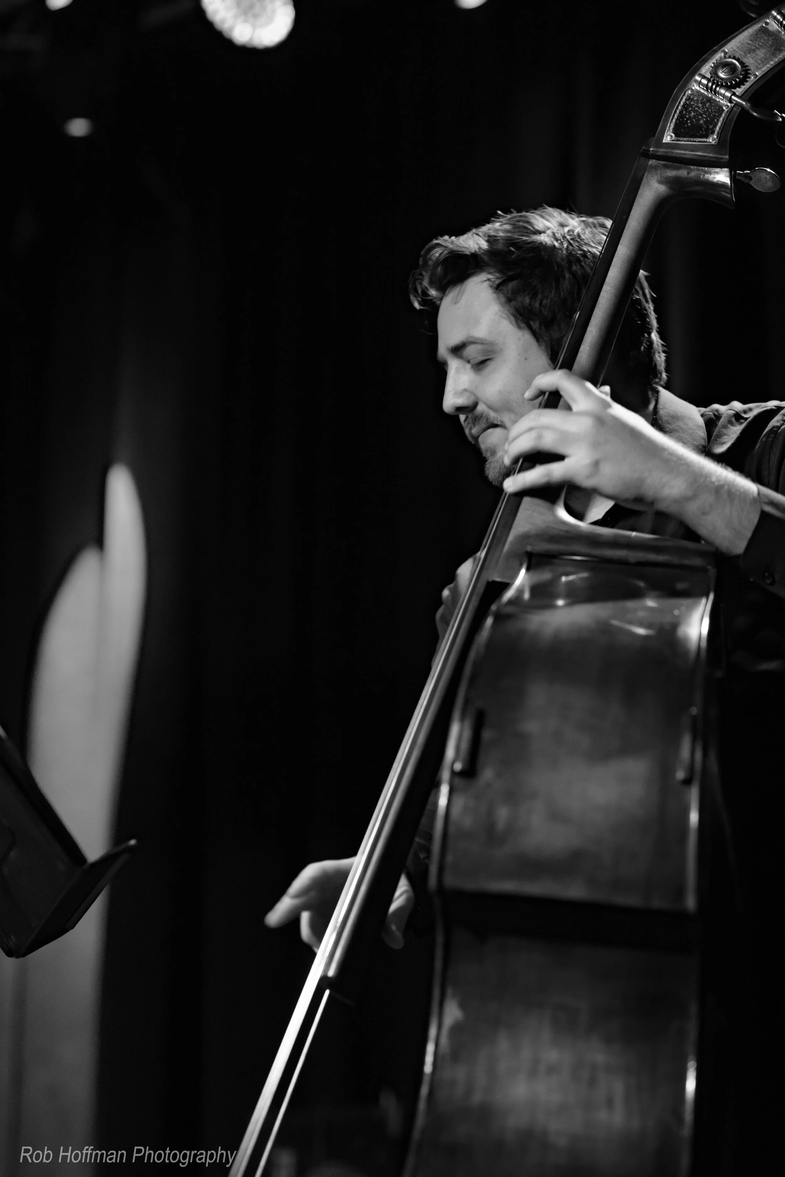 A man playing a double bass on stage, with eyes closed and a focused expression, black and white photo.