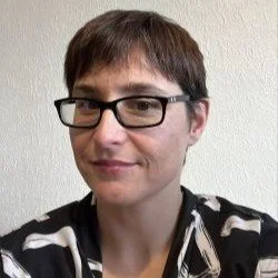 Person with short brown hair and glasses smiling at the camera