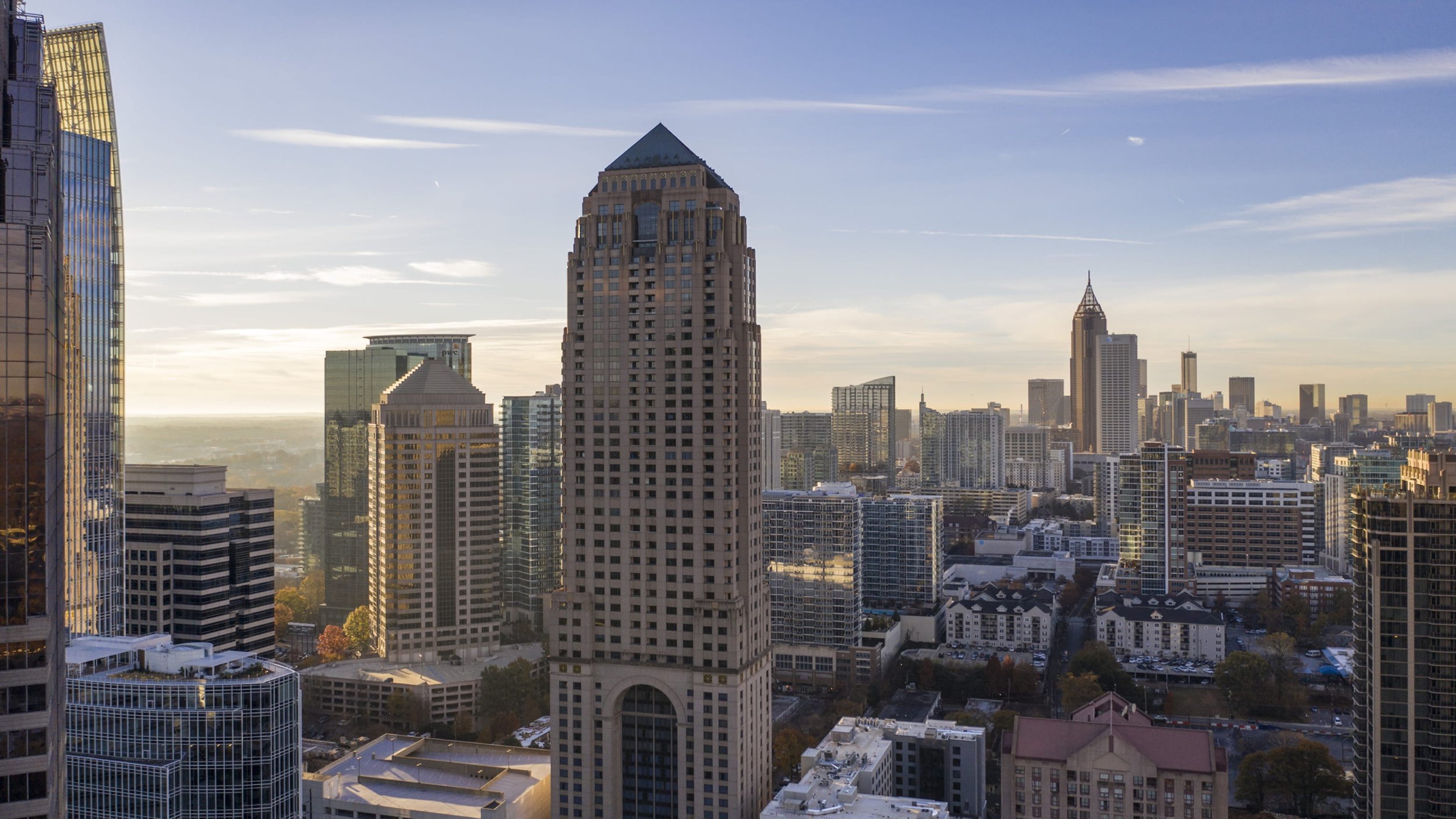 City skyline with tall skyscrapers including a prominent historical building with a pointed roof, under a clear sky with some clouds.
