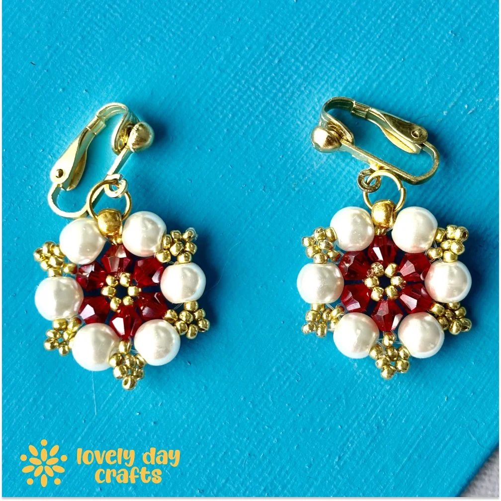 White, red, and gold adriana earrings with starburst variation, made by lovelydaycrafts and photographed on blue background.