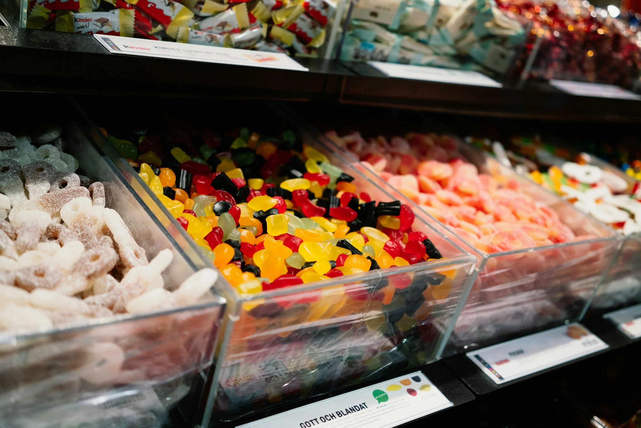 Clear bins filled with assorted colorful candies, including gummy bears, sour worms, and other gummy candies on store shelves.