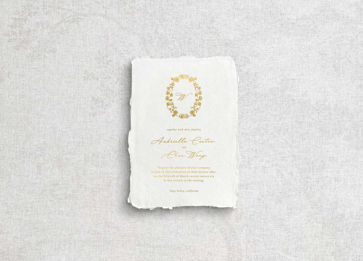 White handmade paper with floral monogram crest and mixed typography with calligraphy printed using gold foil letter press on neutral gray background.