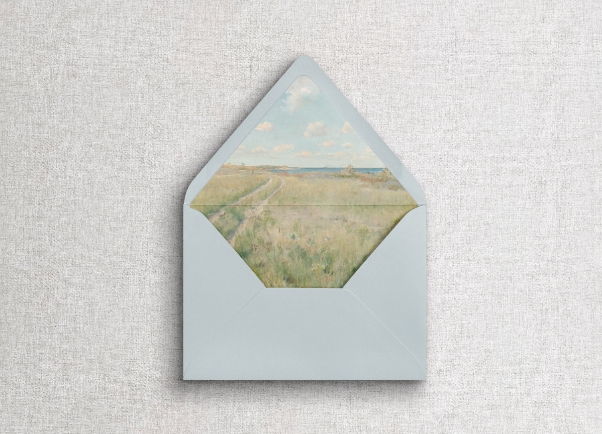 Blue A7 euro flap envelope with misty morning scenic liner on neutral gray background.