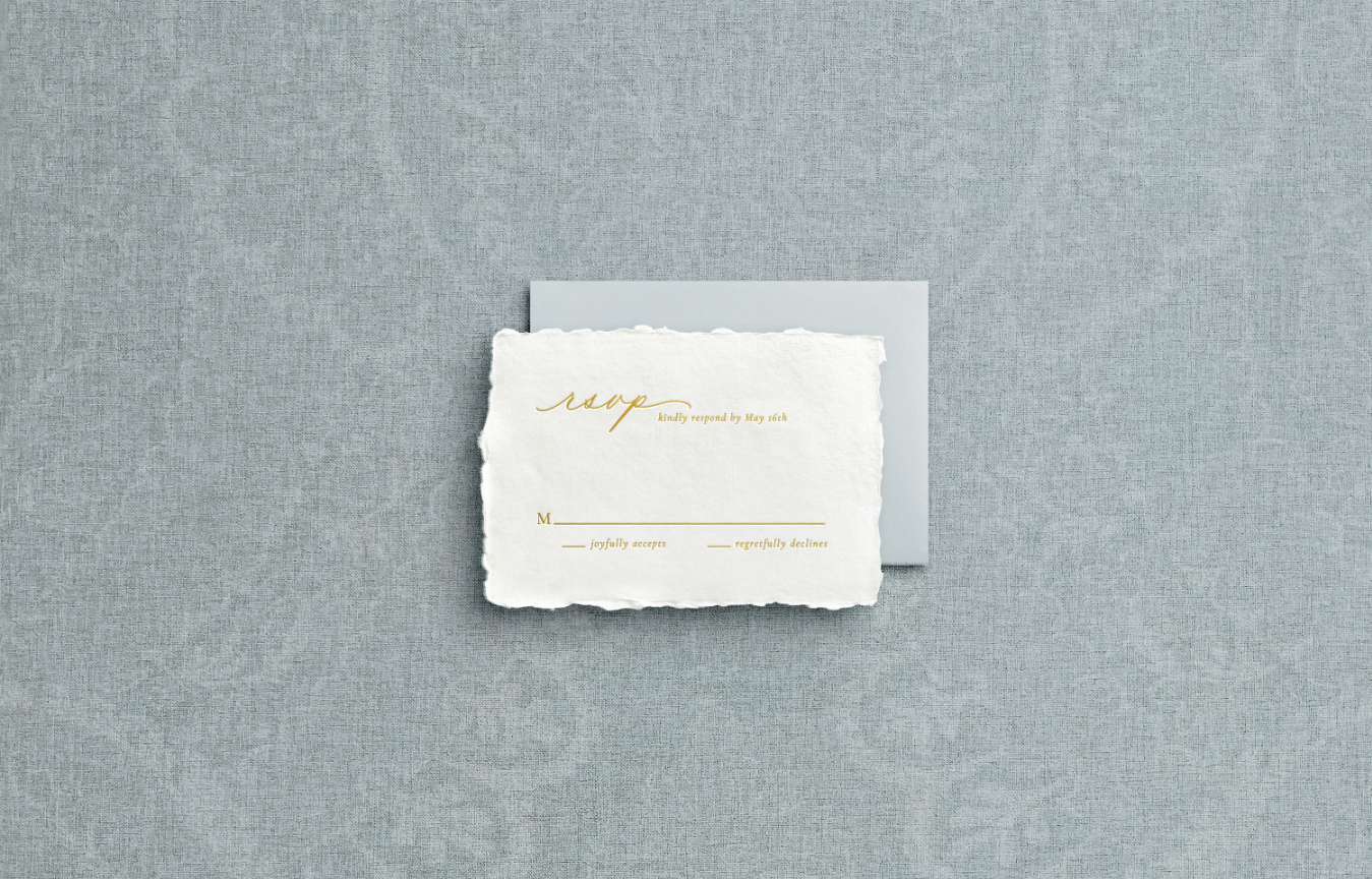 White RSVP card on handmade paper with gold foil letter press with blue return envelope on blue background.