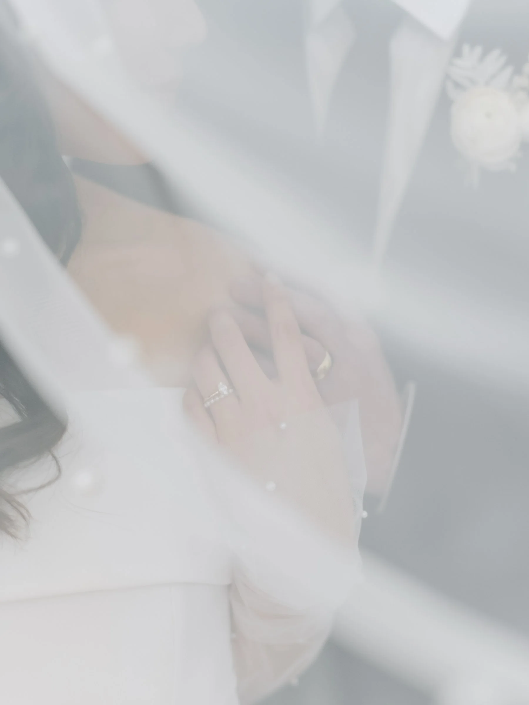 Ethereal close-up of a bride and groom embracing under a delicate pearl-embellished veil.