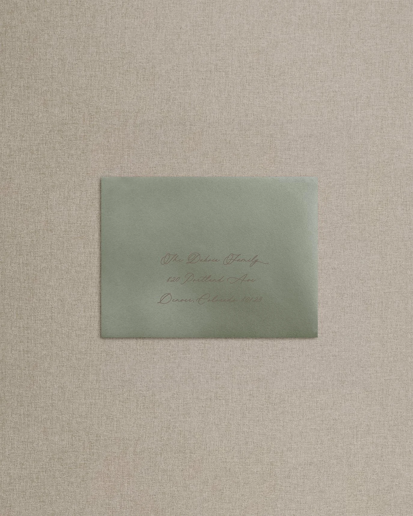 Calligraphy addressing in brown ink on muted green envelope and neutral brown background.