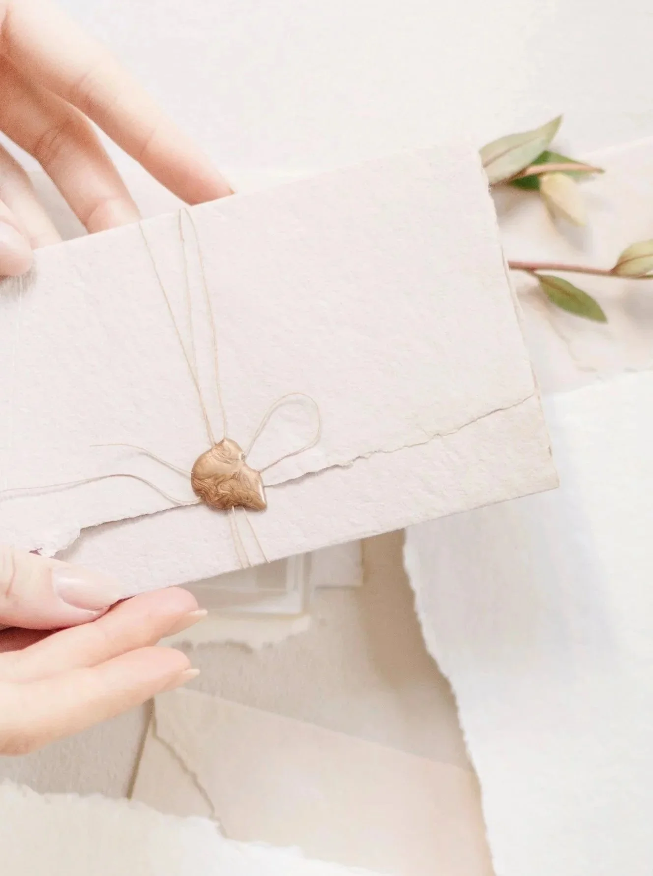 Flatlay of luxury wedding stationery featuring handmade paper with deckled edges, custom wax seals, and hand-dyed silk ribbon