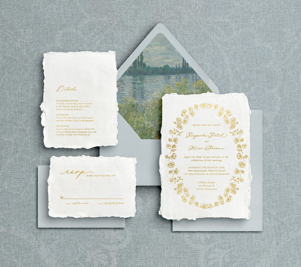 Signature botanical wedding stationery with gold calligraphy, floral border, and dusty blue envelopes on textured handmade paper.