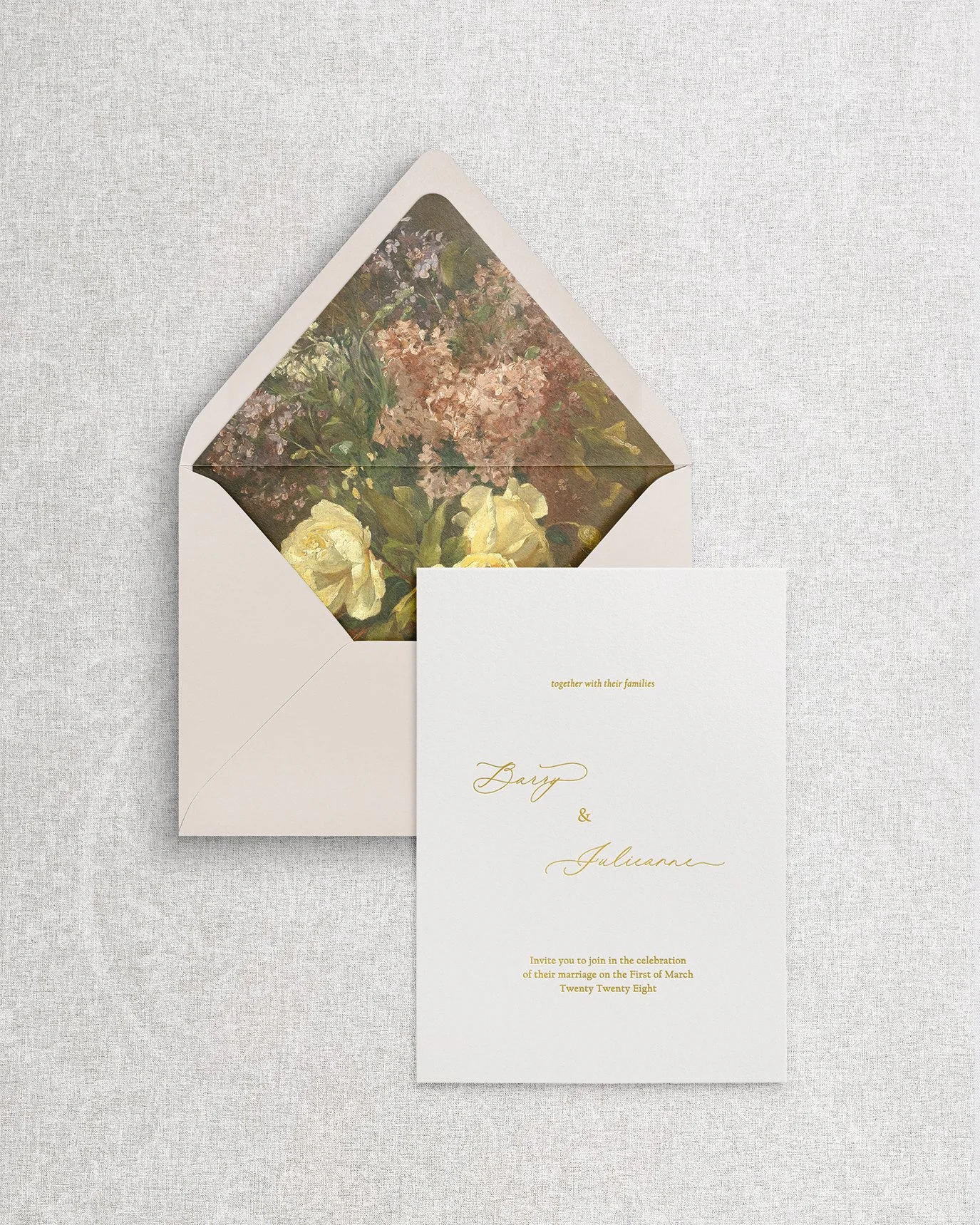 An elegant, simple wedding invitation featuring gold foil calligraphy on premium cardstock, displayed with an open envelope showcasing a romantic floral liner.