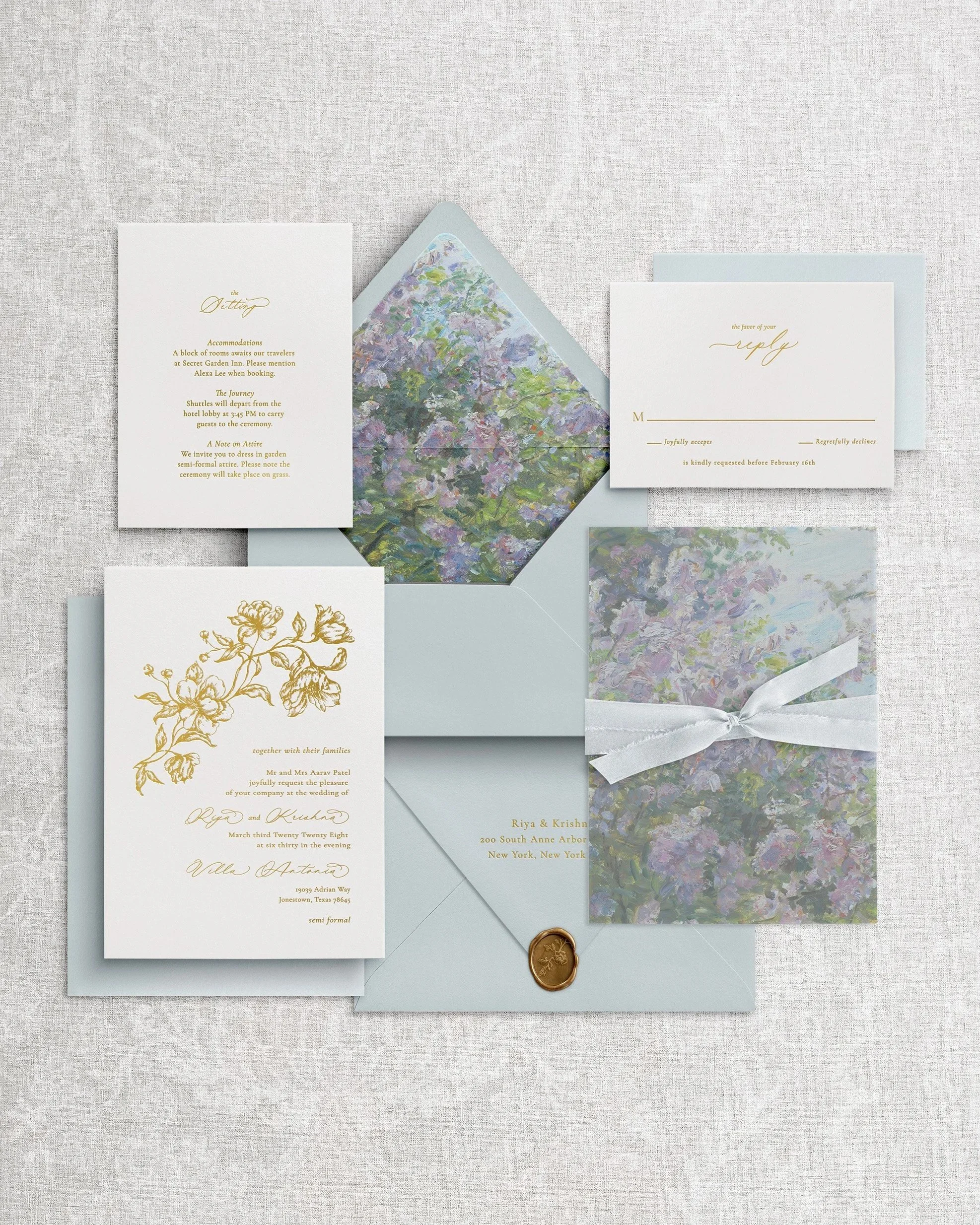 Premium wedding invitation: white cotton cardstock with floral debossing and gold foil letterpress calligraphy, plus a vellum wrap, dusty blue silk ribbon, and a matching wax seal on gray background.