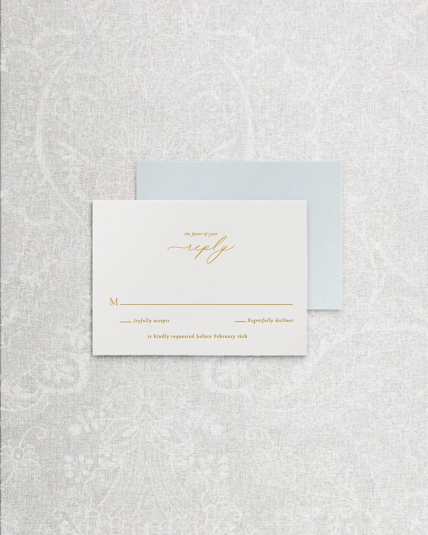 An elegant and simple wedding invitation RSVP card featuring gold foil calligraphy on white cardstock, paired with a light blue envelope.