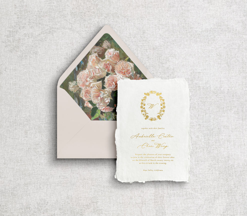 Champagne beige envelope with floral liner, main invitation on white handmade paper with floral monogram crest and calligraphy printed using gold foil letter press on neutral gray background.