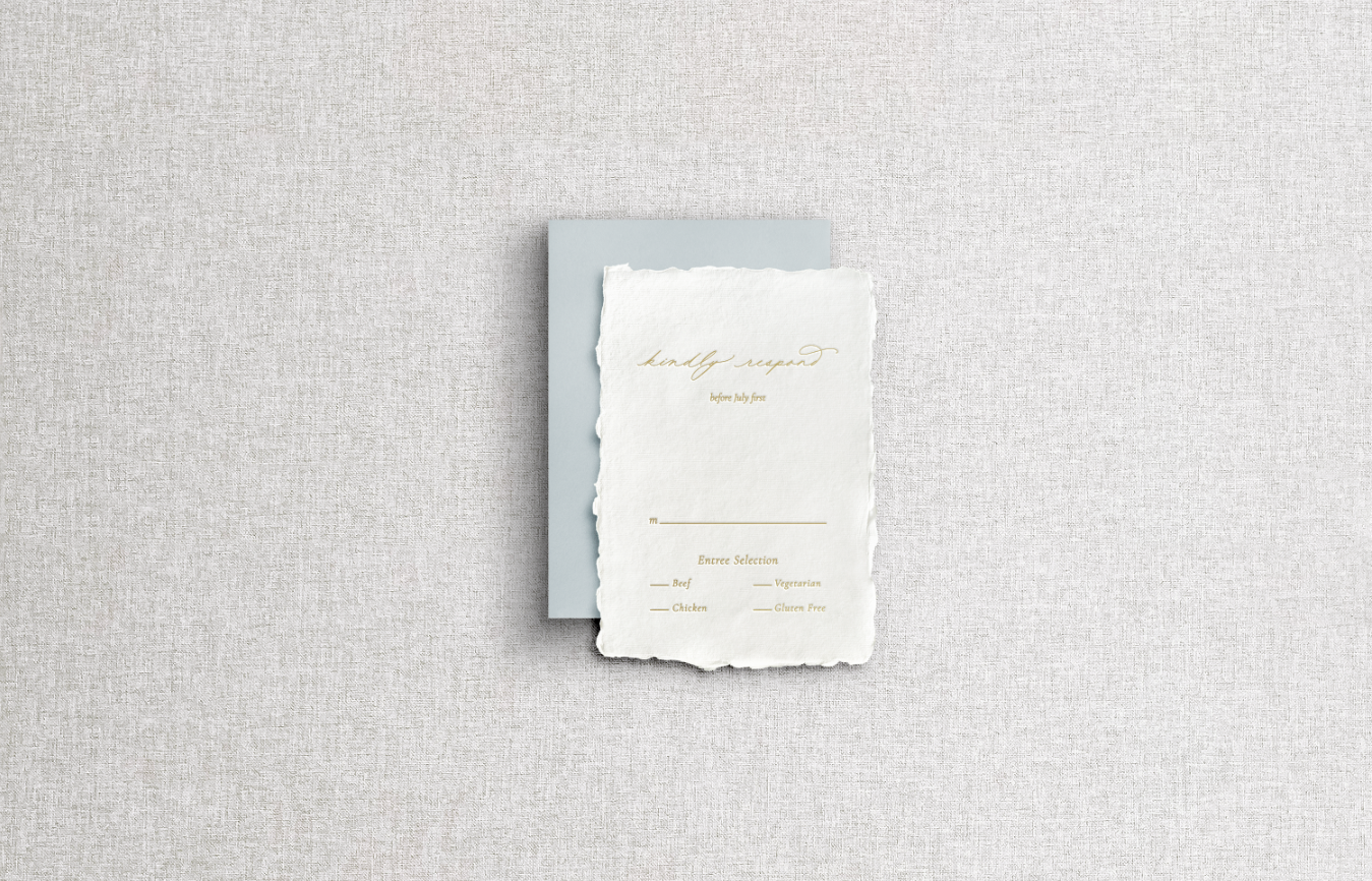 RSVP card on handmade paper with mix typography including calligraphy using gold foil letter press and blue return envelope on neutral gray background.