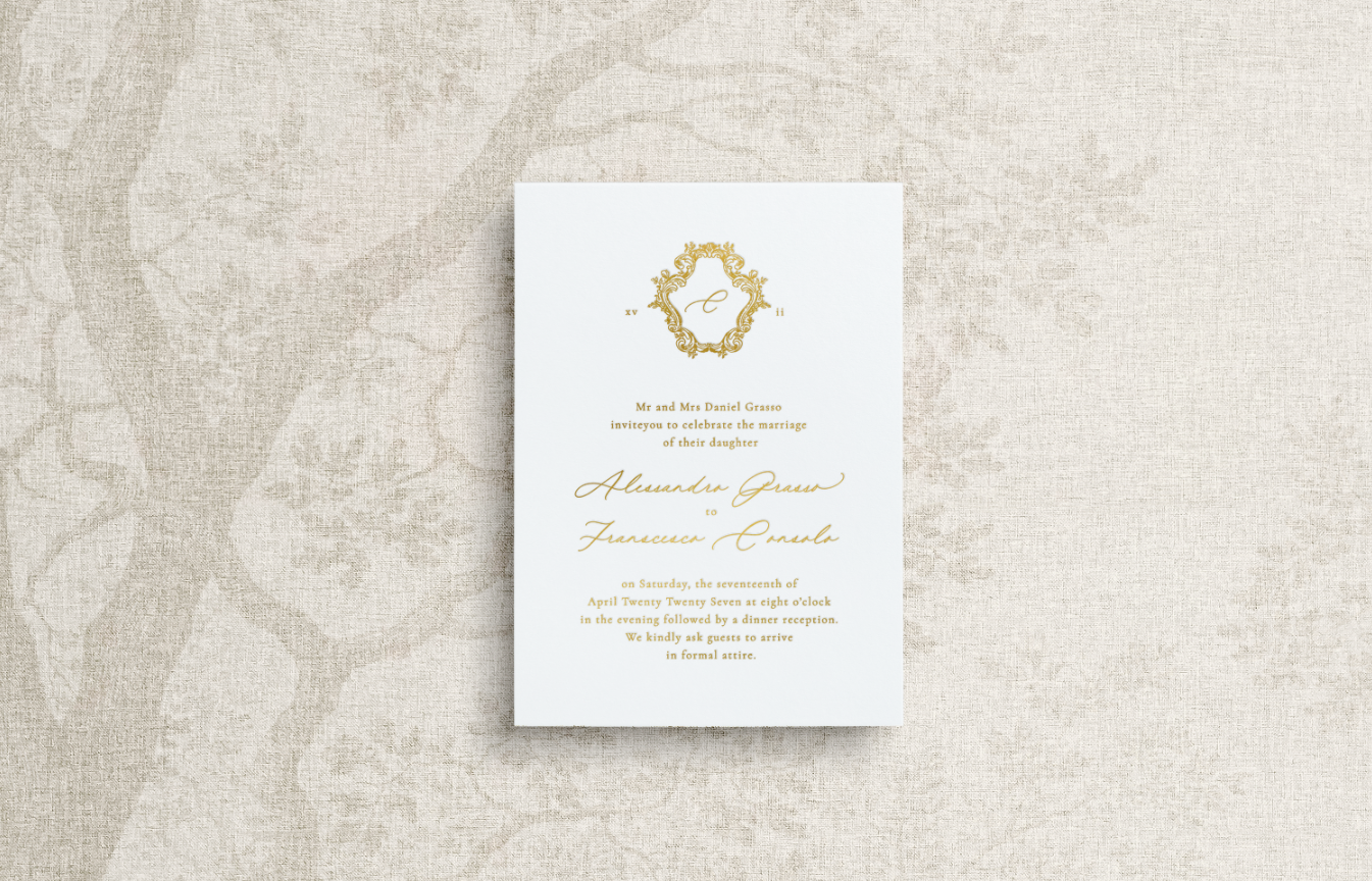 An elegant and simple wedding invitation featuring gold foil calligraphy and an ornate monogram crest.