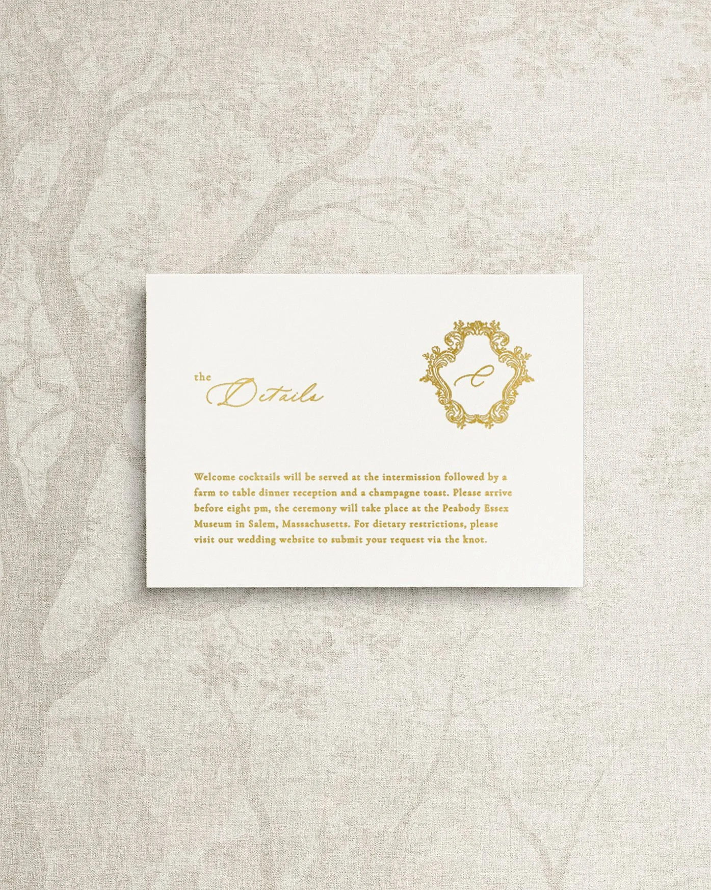 An elegant and simple wedding invitation details card featuring gold foil calligraphy and an ornate monogram crest.