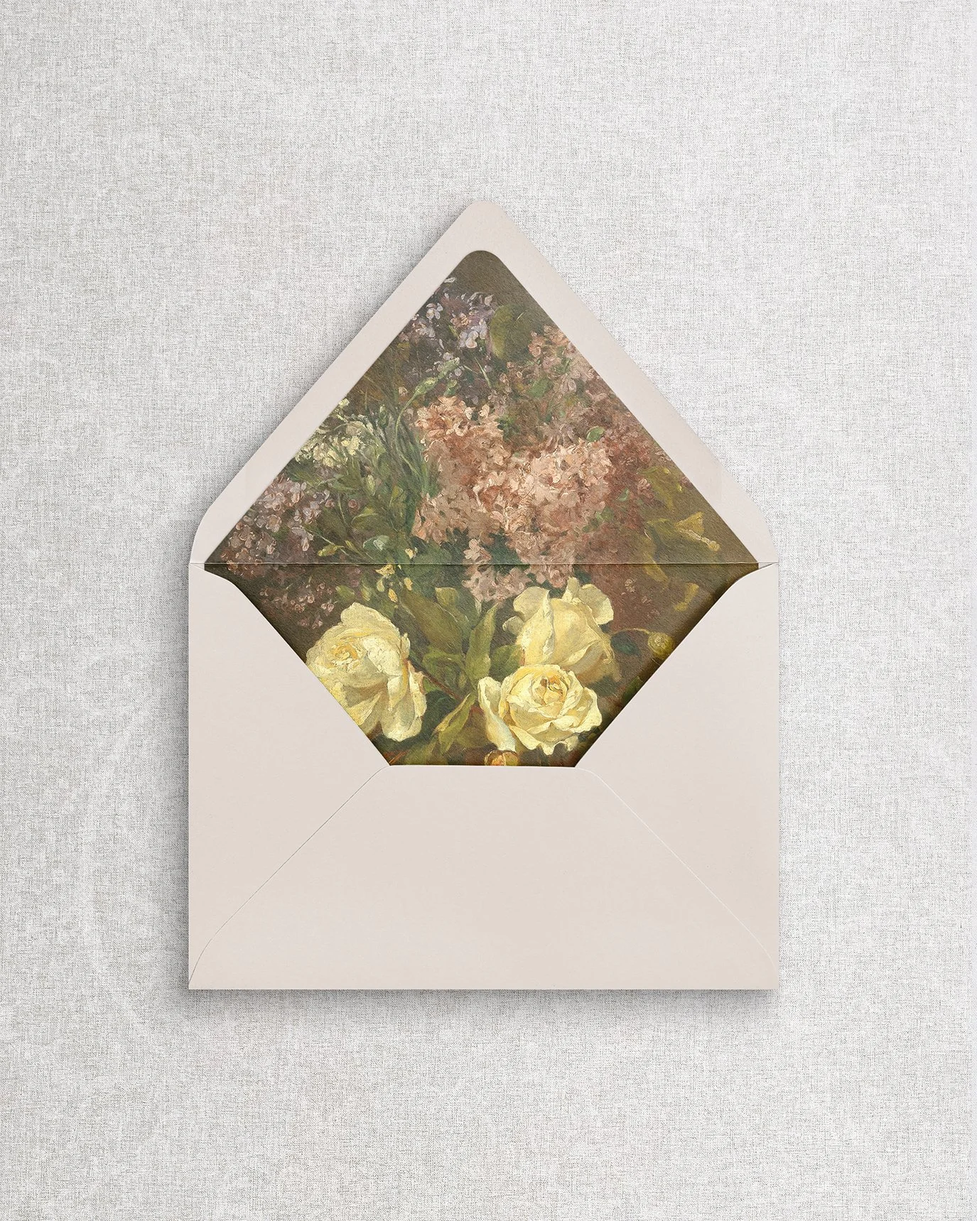 Close-up of a champagne beige wedding envelope open to reveal a vibrant, fine art floral printed envelope liner featuring muted green and pink tones.