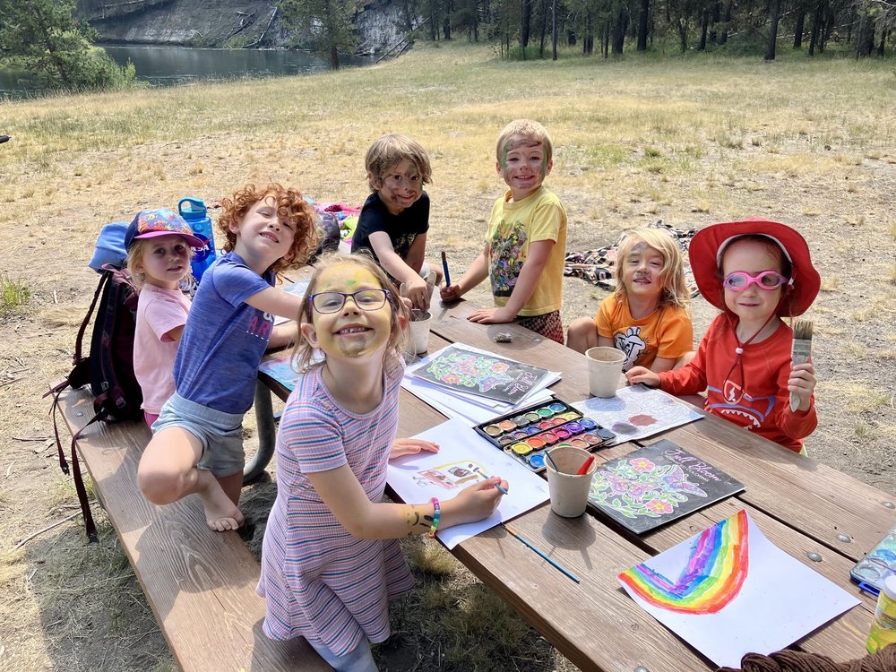 Campers drawing colorful artwork at a picnic table in the forest
