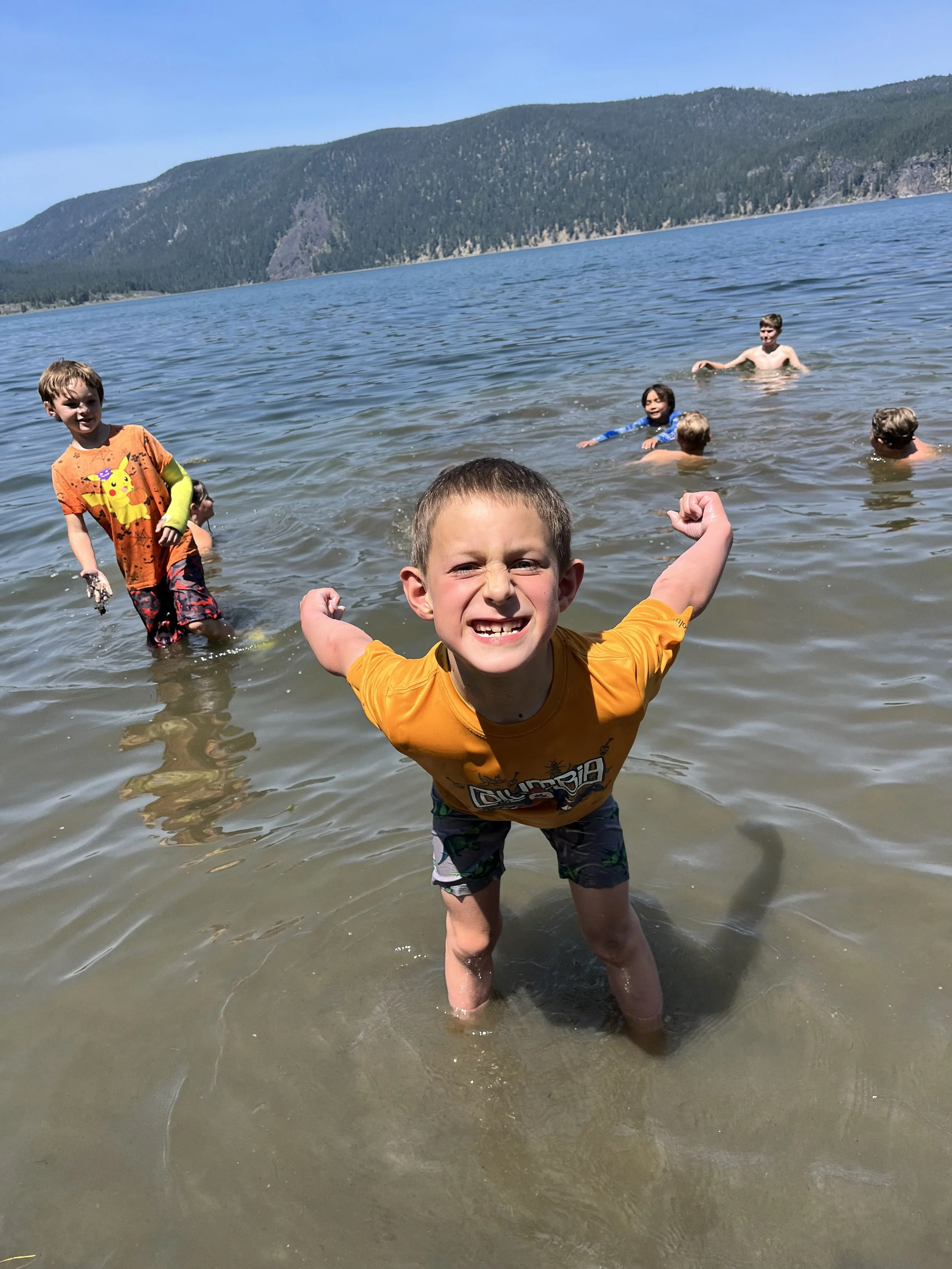Children playing and swimming in a lake with mountain scenery in the background.