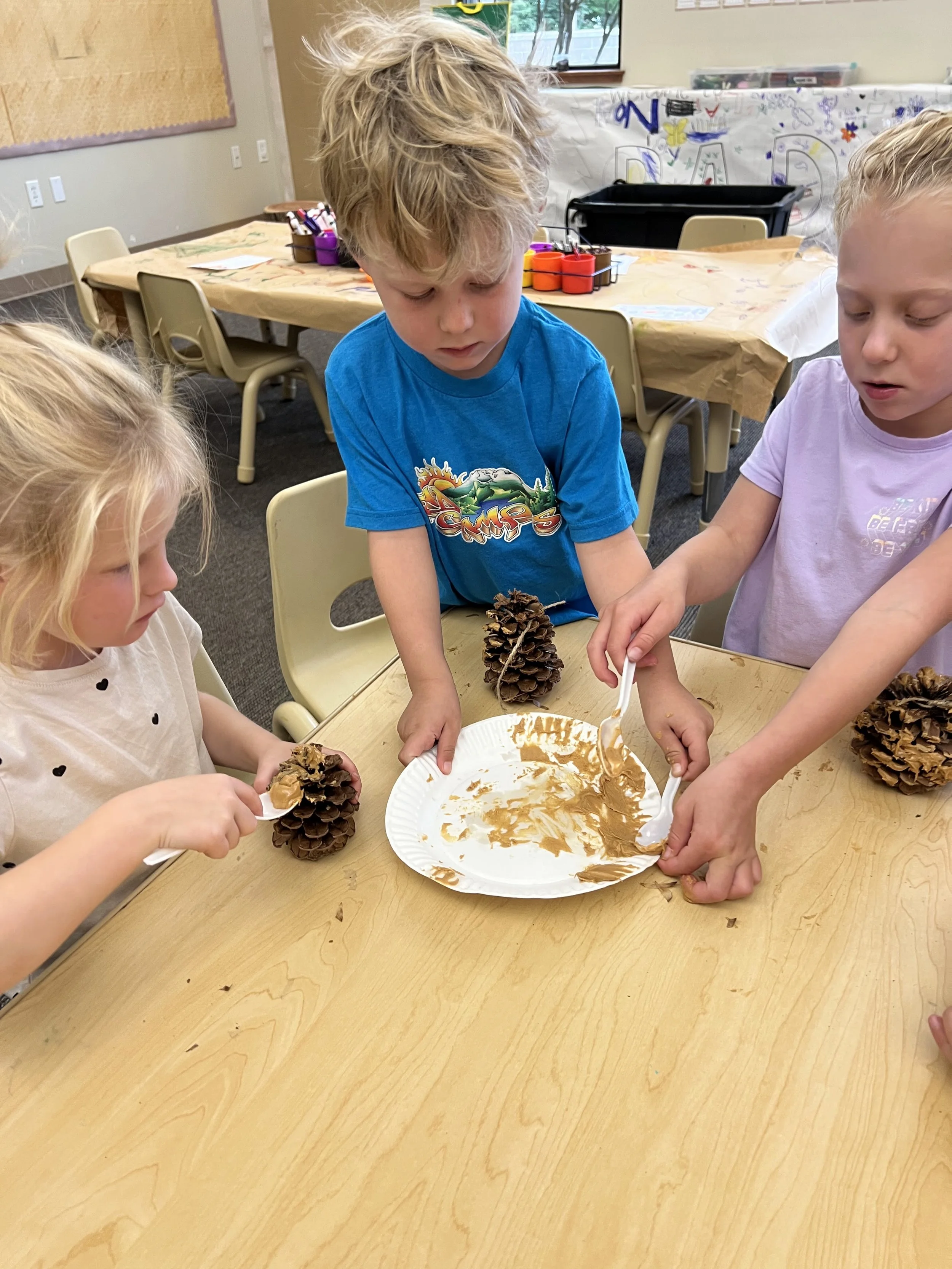 Children at a table decorating pine cones with peanut butter and birdseed.
