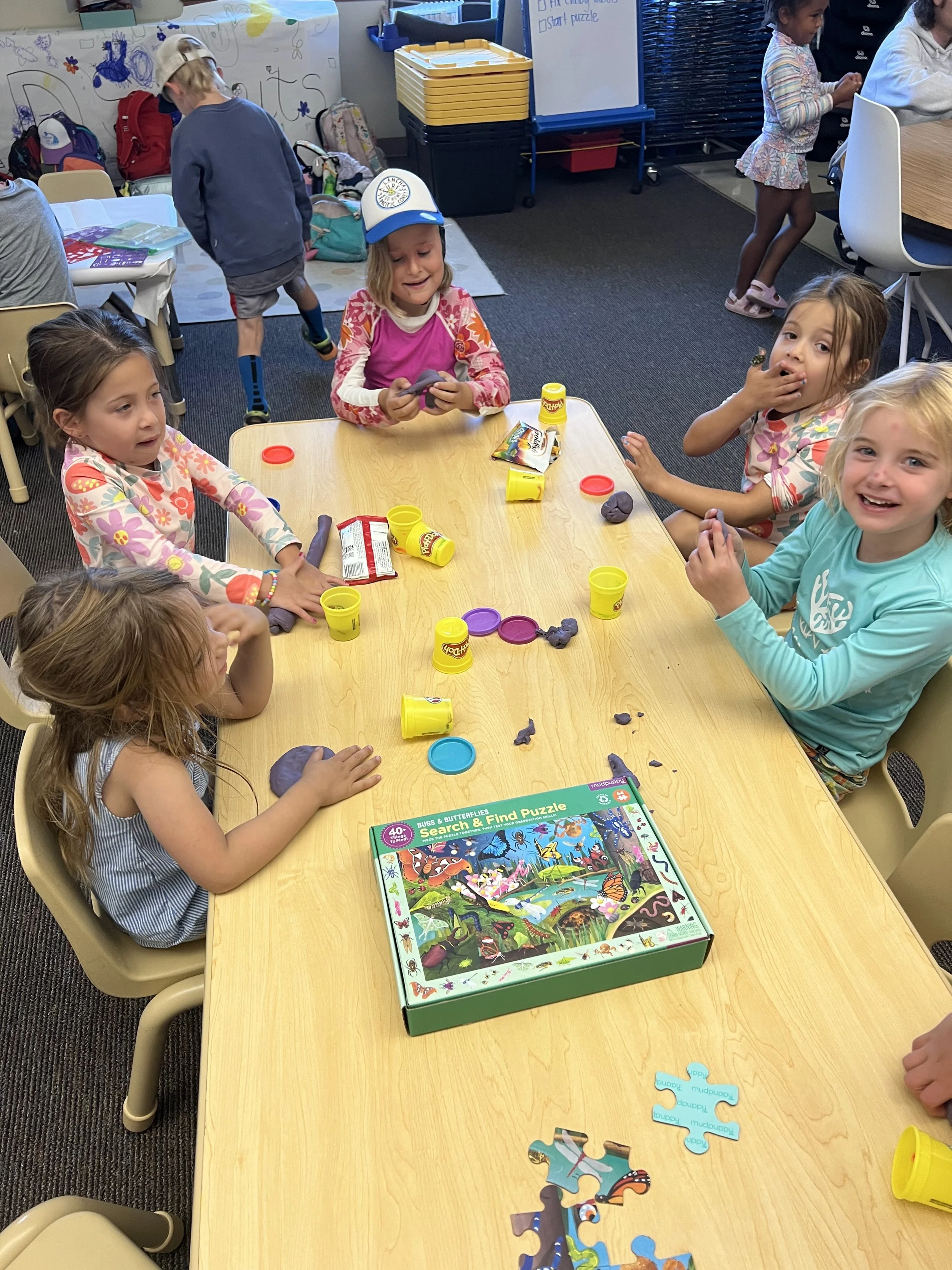Children playing with modeling clay and completing a puzzle at a classroom table.