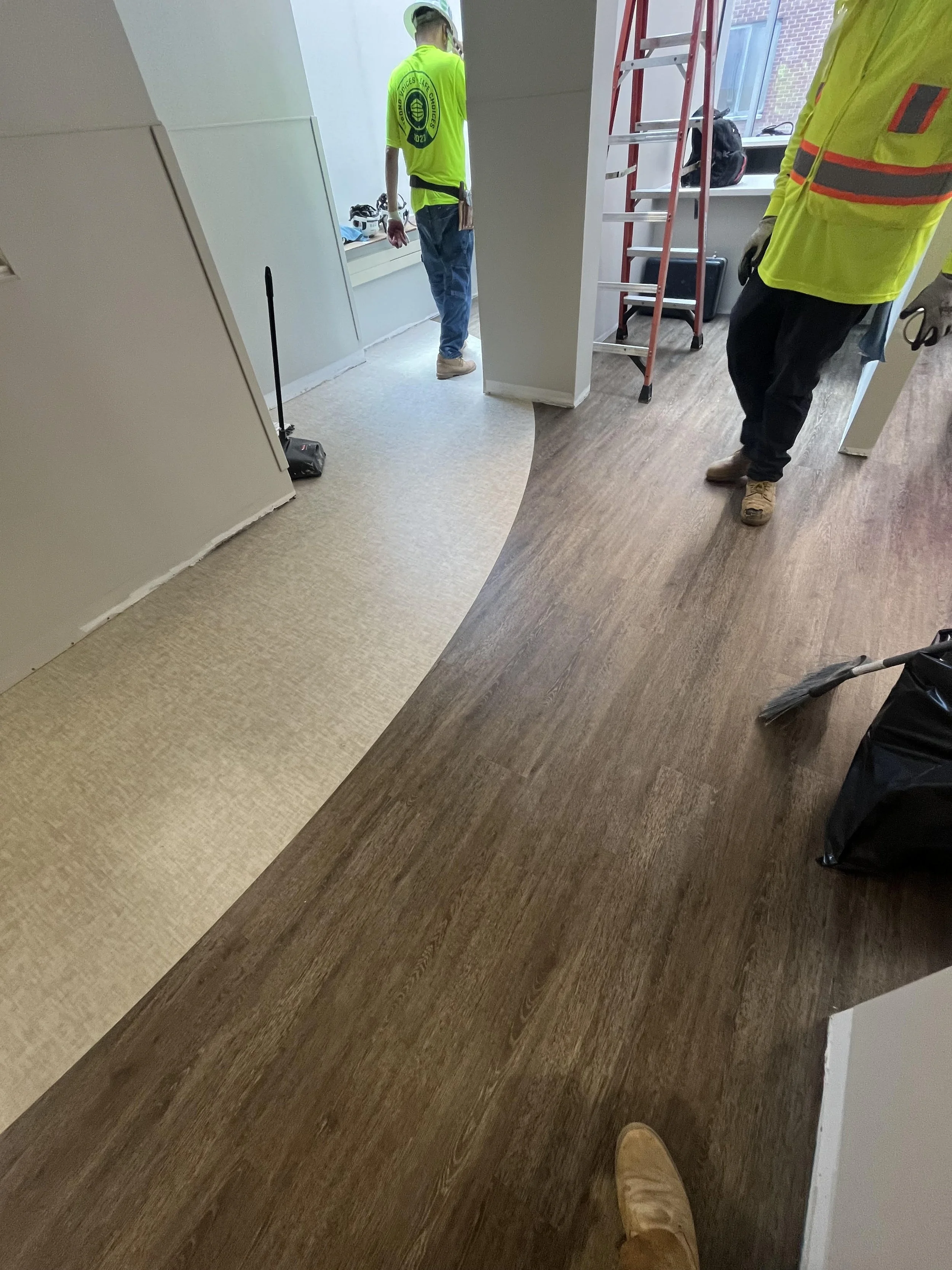 Workers installing or repairing flooring in an office space with a transition from beige carpet to wood flooring.