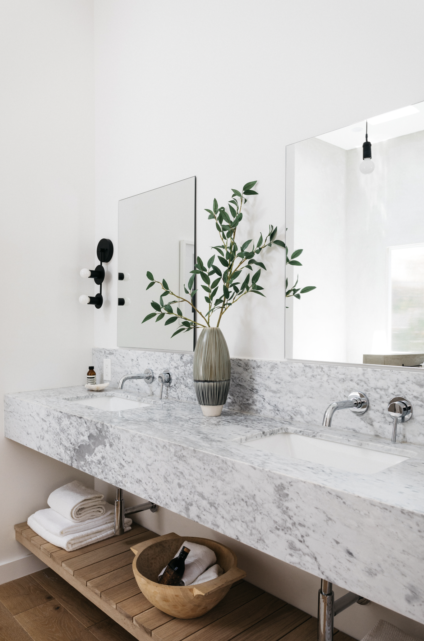Modern bathroom vanity with a marble countertop, a large mirror, and a green leafy plant in a striped vase.
