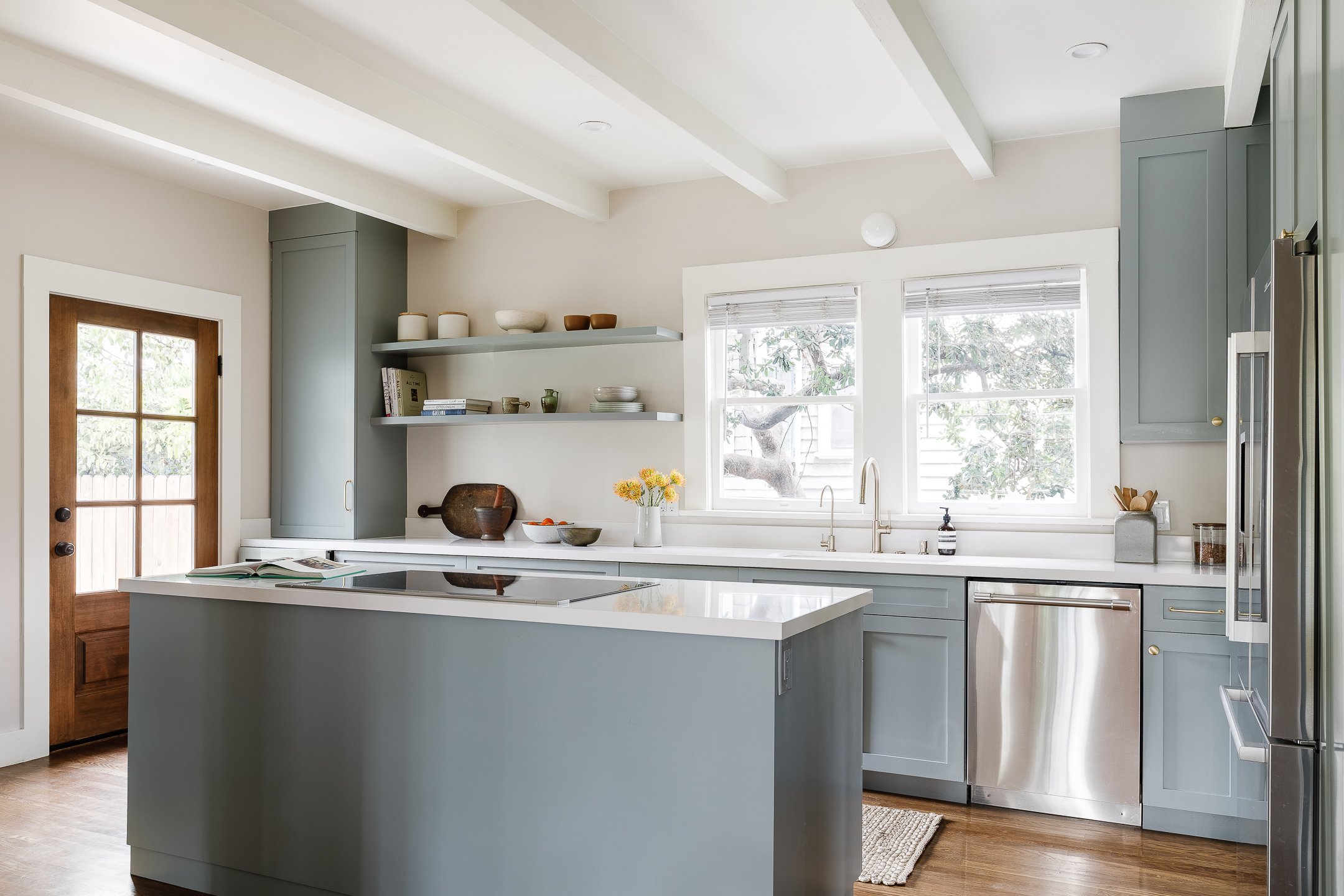A modern kitchen with blue cabinets, white countertops, a small kitchen island, and large windows.