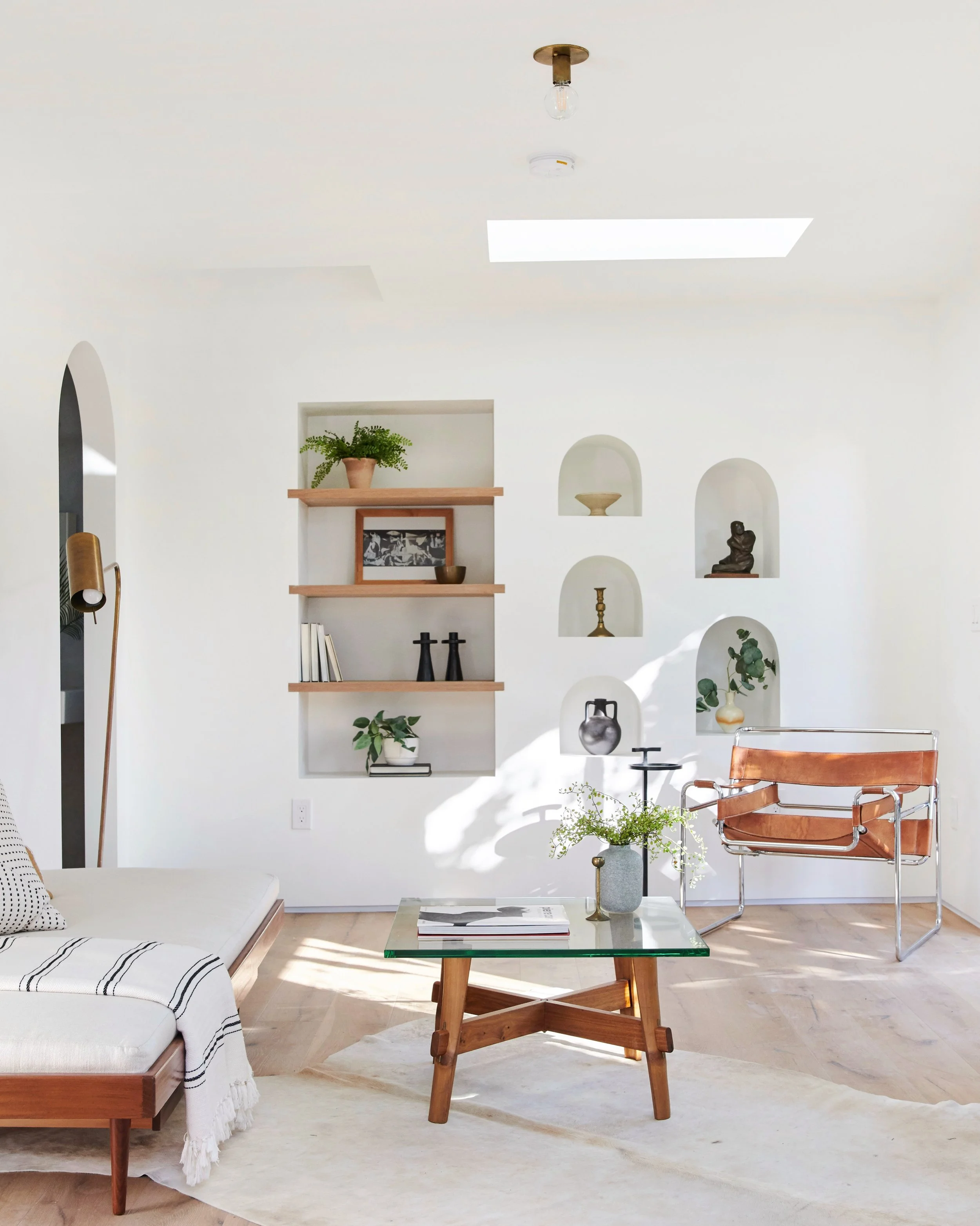 Modern living room with white walls, wooden furniture, and decorative shelves with plants and art.