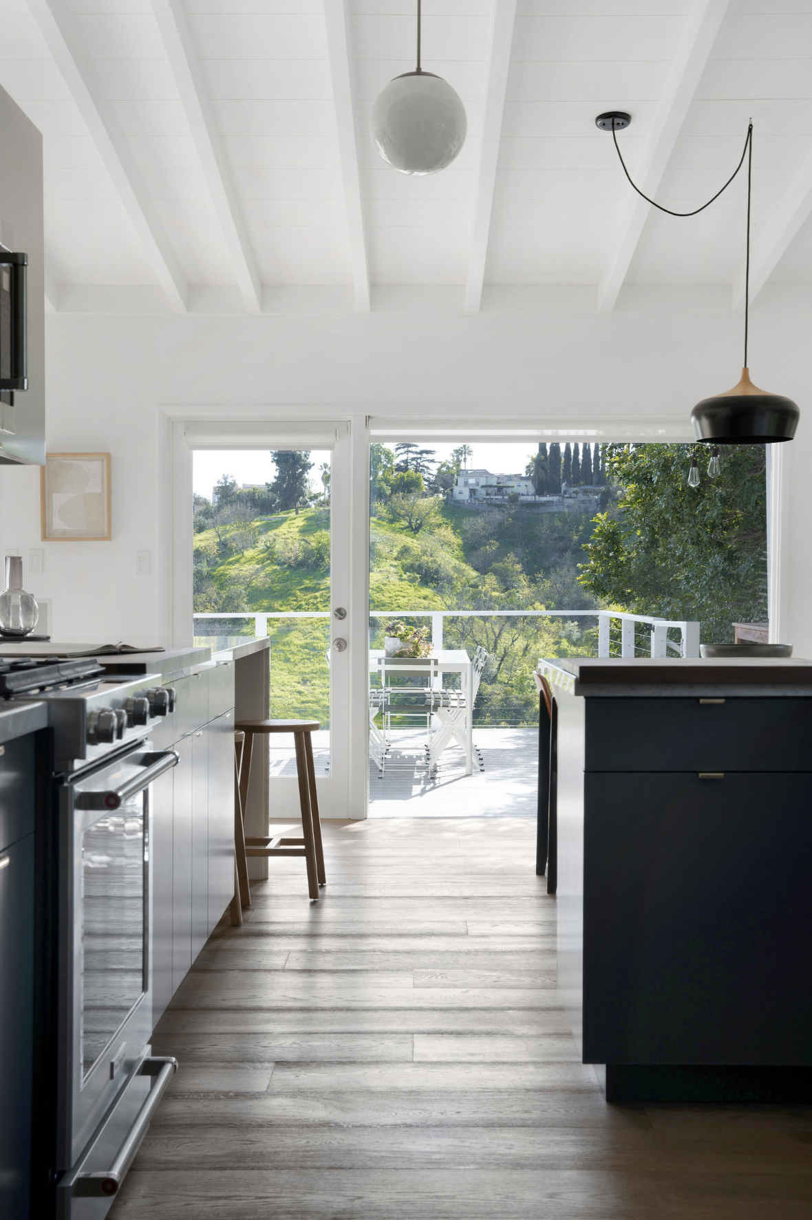 Modern kitchen with a view of a green hillside and a balcony with outdoor furniture.
