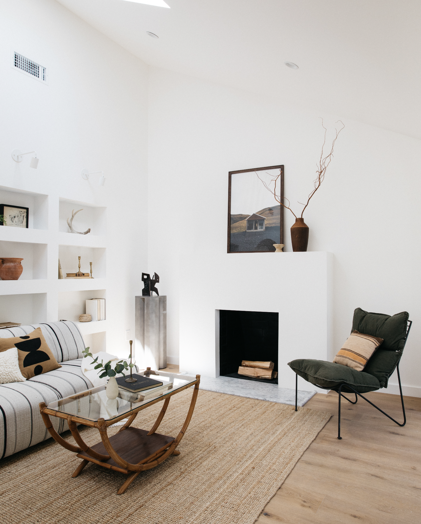 Living room with a white sofa, glass coffee table, black armchair, fireplace, and decorative vases and artwork.