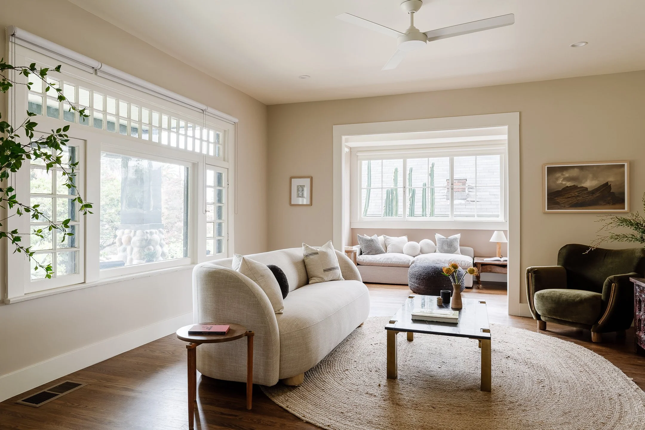 Bright living room with large windows, white sofas, a coffee table, and a mix of modern and vintage decor.