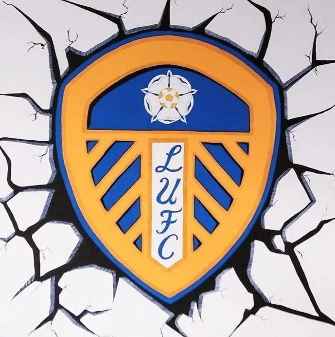 A wall with the emblem of Leeds United Football Club painted to look like it is breaking through, featuring a shield with a yellow and blue design and the club's initials 'LUFC' on a white vertical banner.