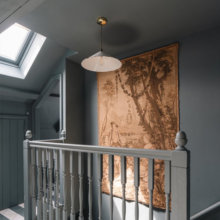 Interior view of a staircase landing with a large tapestry hangin on the wall, a white railing, gray walls, and a skylight.