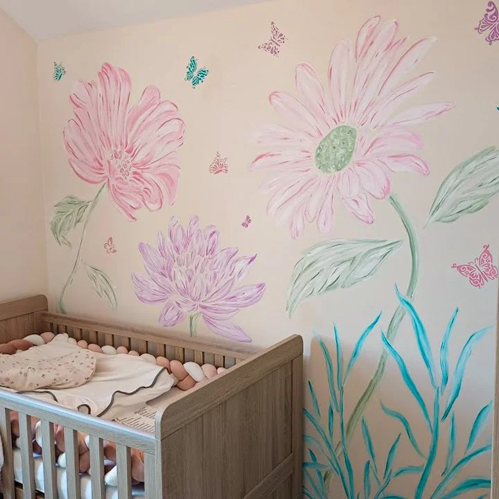 Nursery room with hand-painted large pink and purple flowers and butterflies on the wall, wooden crib with pink, white, and beige bedding.