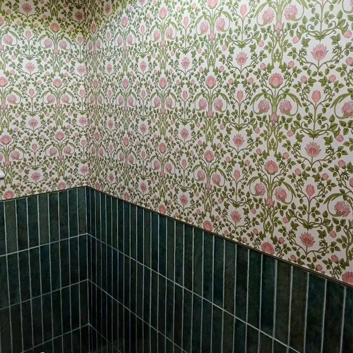 Corner of a room with floral wallpaper featuring pink flowers and green vines, with dark green tiled lower wall.