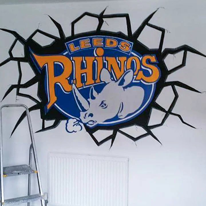 Logo of the Leeds Rhinos rugby team featuring a white rhinoceros head and the team name, on a wall with a cracked black design surrounding it.