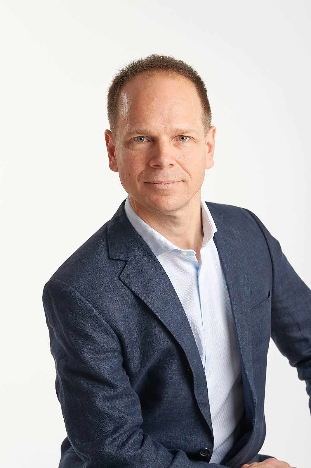 Professional headshot of a man in a navy blue blazer and white shirt against a white background.
