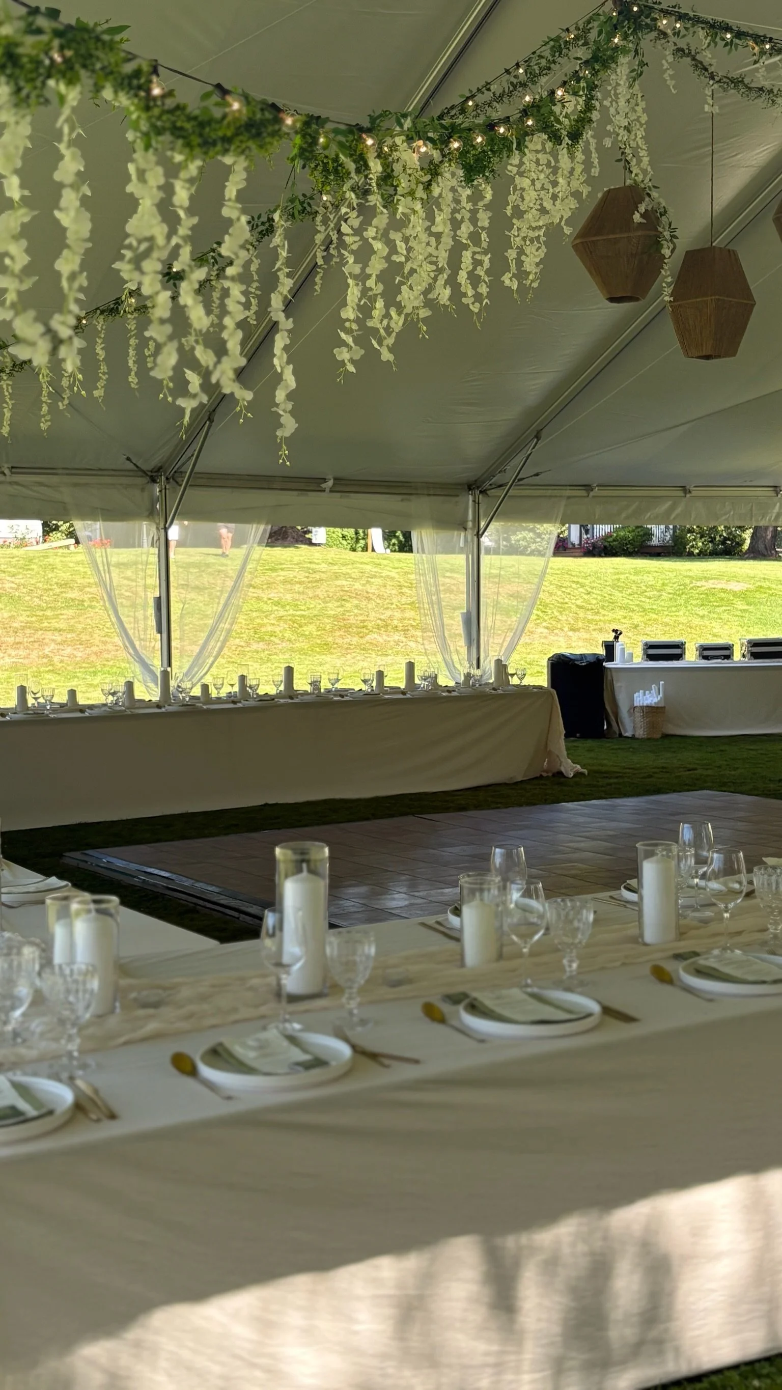 Wedding reception setup inside a tent with decorated tables, hanging floral arrangements, and a head table with white drapes and candles.