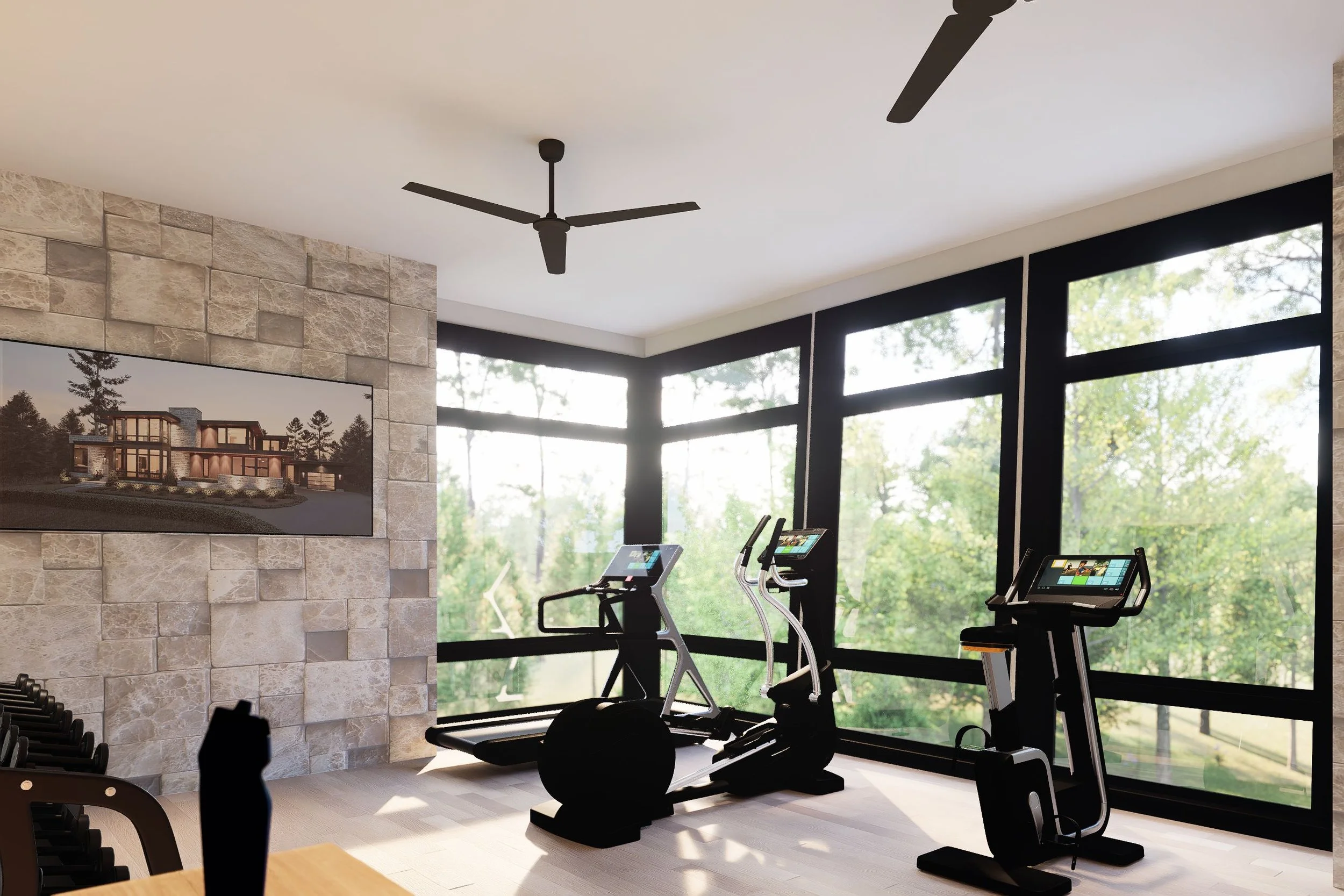 A modern home gym with treadmills, elliptical machines, and exercise bikes near large windows overlooking trees, with a stone accent wall and a ceiling fan.