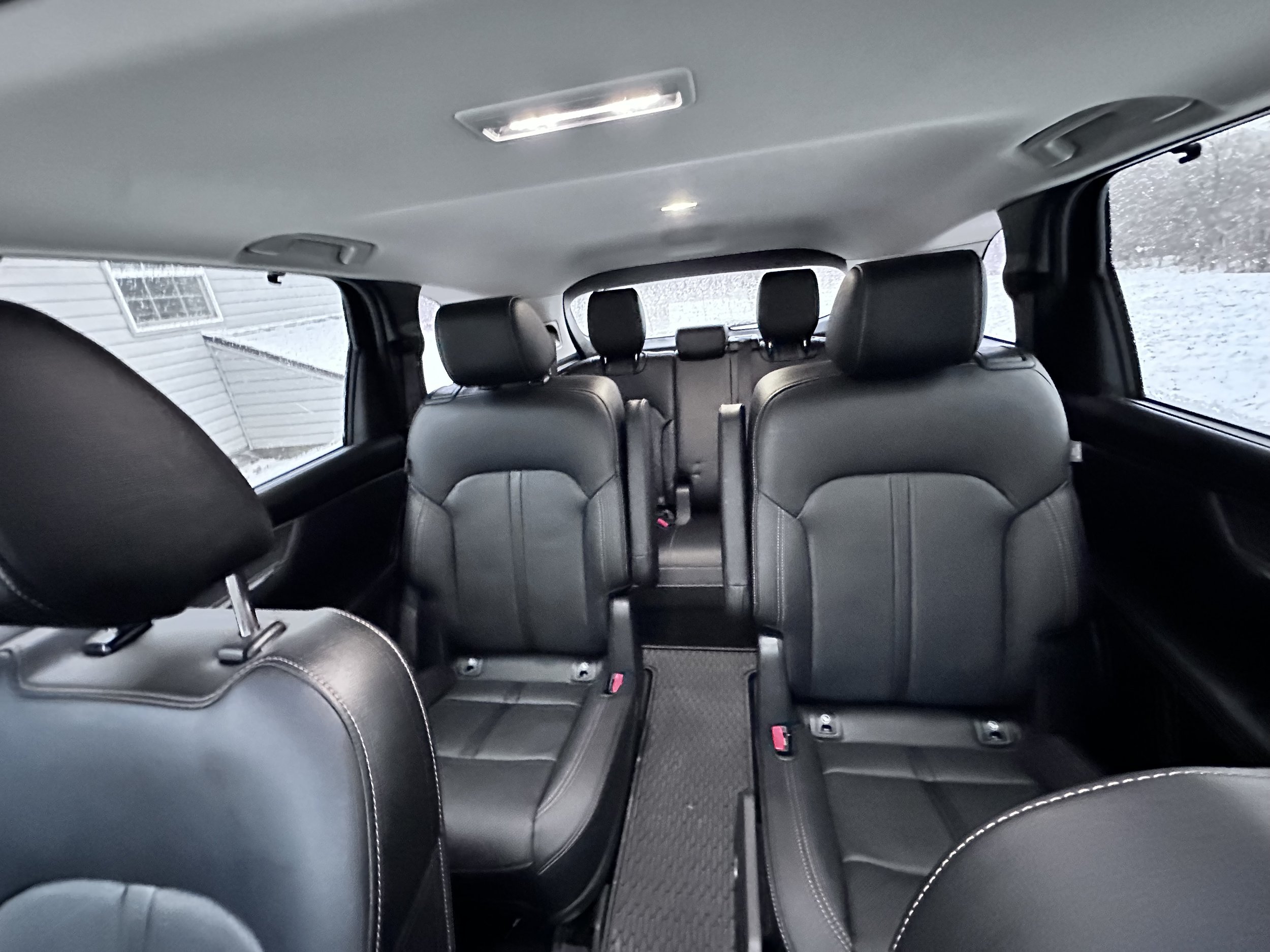 Interior of a vehicle showing three rows of black leather seats, with headrests, in a snowy outdoor environment