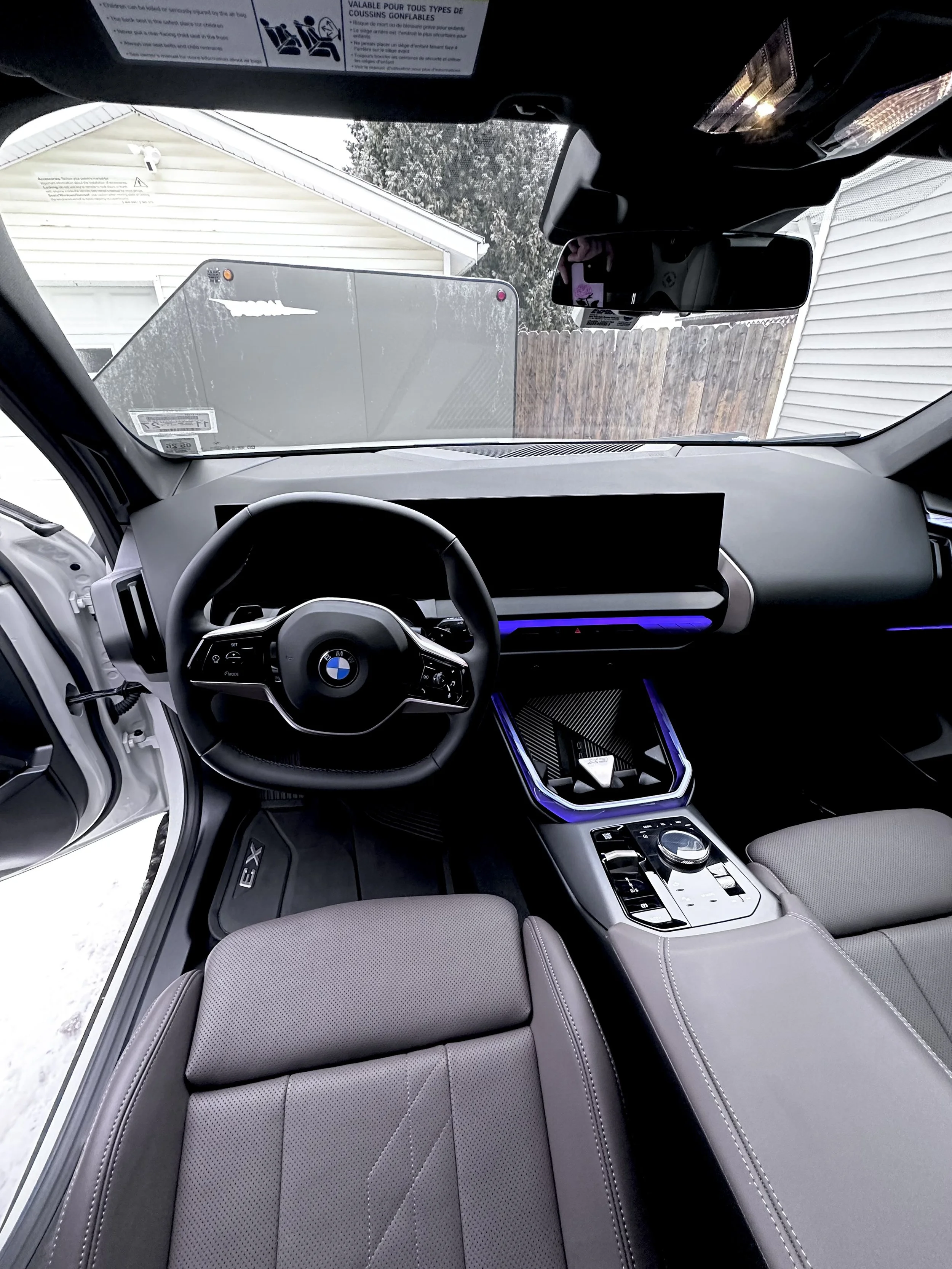 Interior of a modern BMW vehicle with a digital dashboard, steering wheel, center console with electronic controls, and gray upholstery seats.