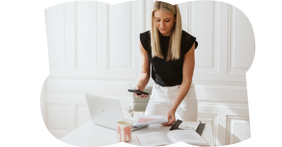 Frau arbeitet an einem weißen Schreibtisch mit Laptop, Notizbuch, Stift, Tasse und Papieren in einem hellen Büro.