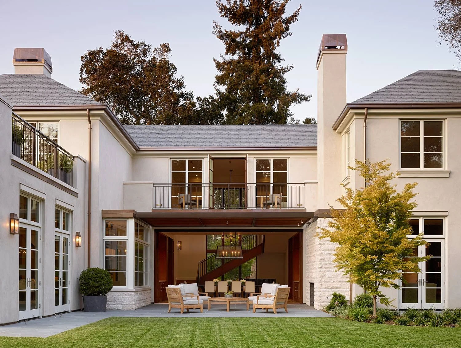 Rear view of a two-story house with a backyard patio, outdoor furniture, and a tree in the yard.
