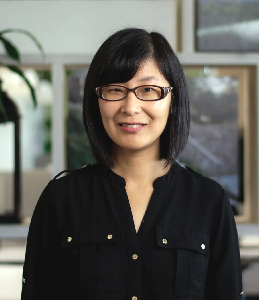 A woman with black hair and glasses smiling in an office setting.
