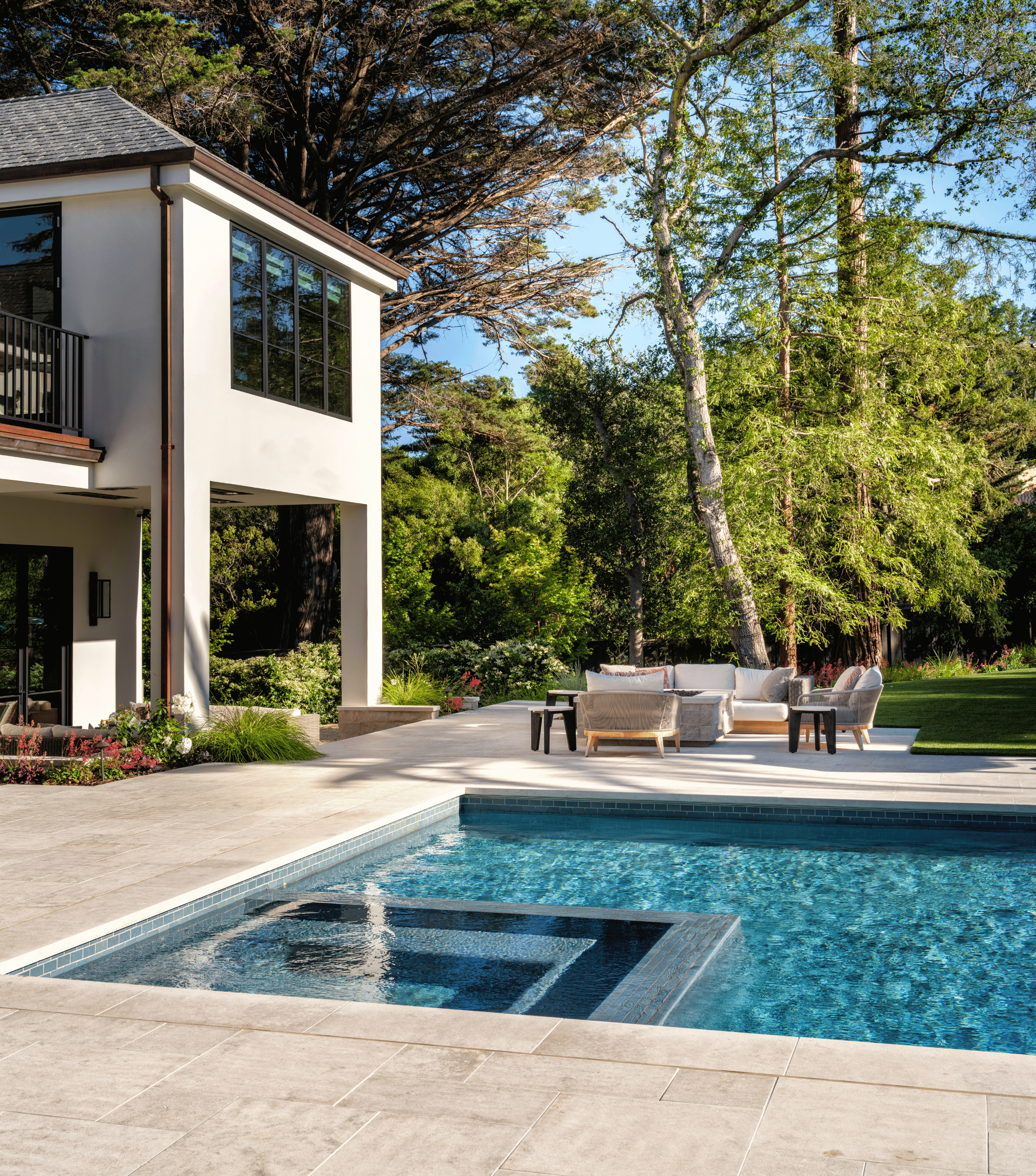 Backyard with swimming pool, outdoor seating area, and modern house surrounded by trees and greenery
