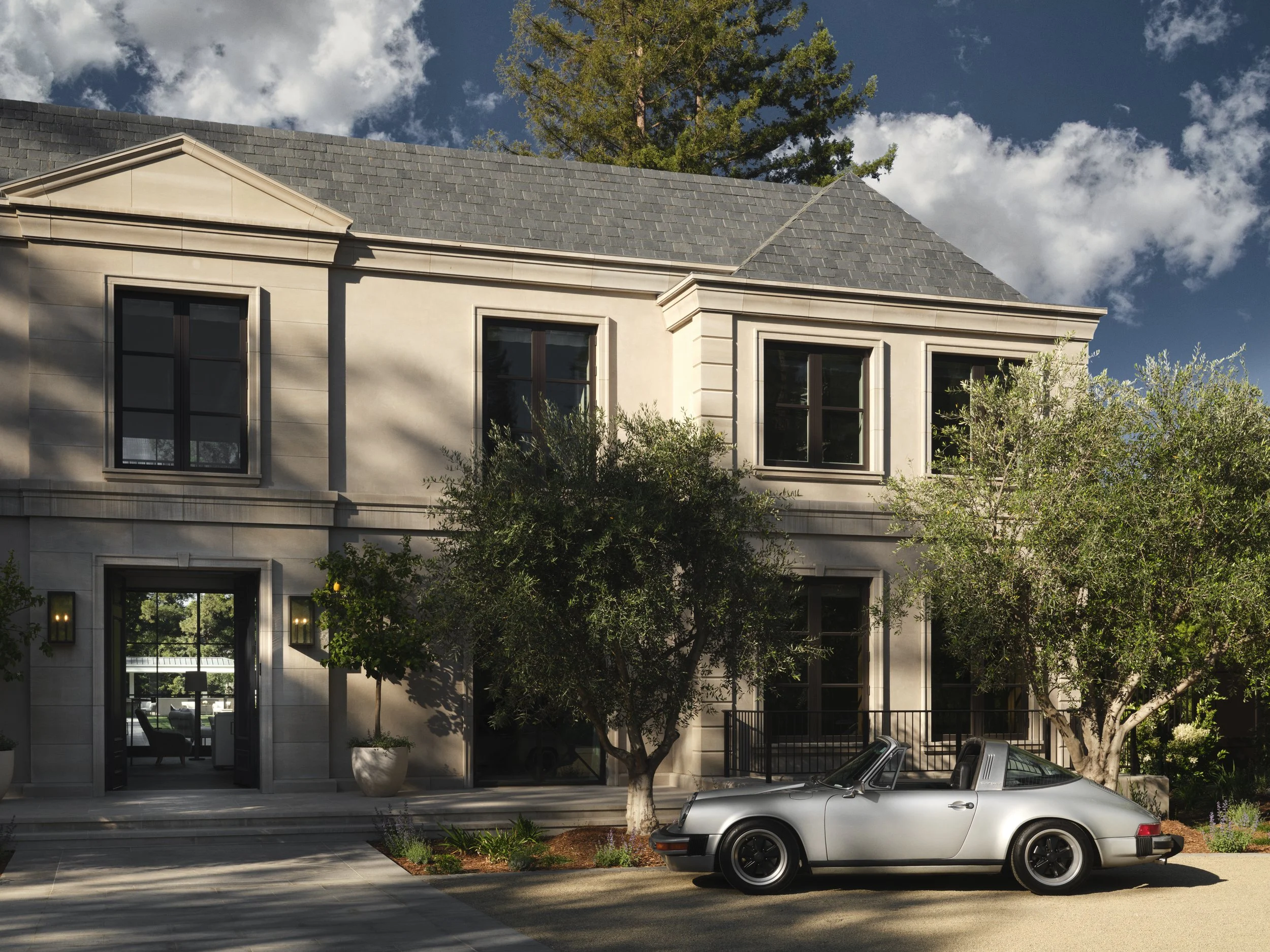 Front view of a modern two-story house with trees and a silver convertible car parked outside.